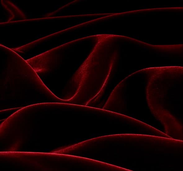 Burgundy velvet raked by low light, the pile throwing long soft folds across the frame.