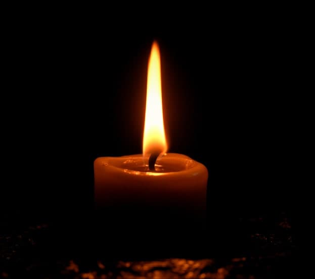 A single lit candle photographed close, the flame the brightest thing in an otherwise black frame.