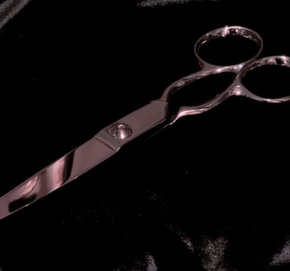 A pair of open scissors lying on black, the blades and finger loops picked out in cold reflected light.