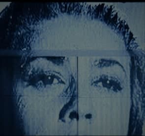 A face from a projected black-and-white film falling across the wall in cold blue, split by the scan lines of the projector.
