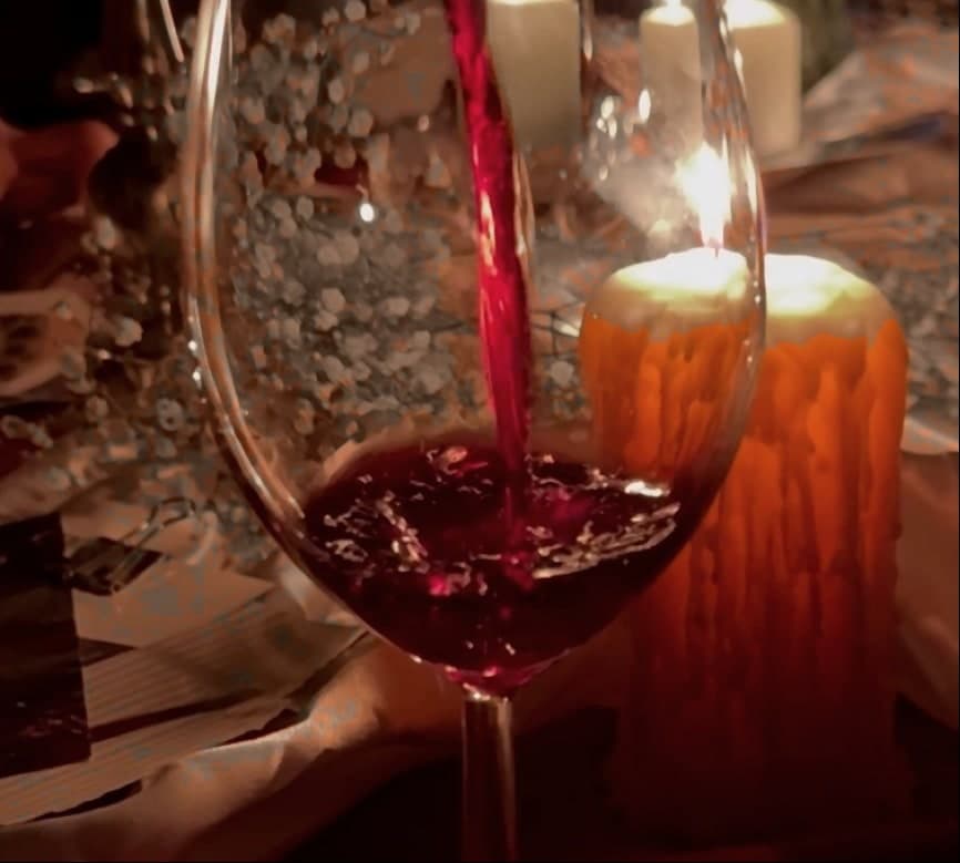 Wine being poured into a glass in front of a burning candle, the stream lit red from behind.
