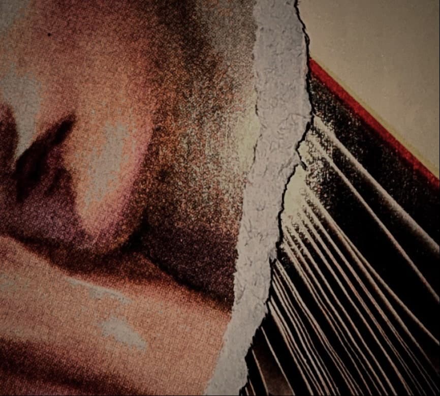 A torn paper edge in extreme close-up over a printed face, the fibres standing up along the tear.