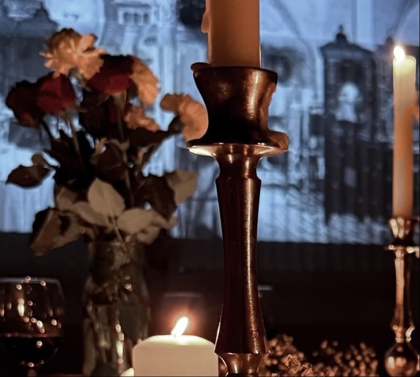 Brass candlesticks and flowers on the table with the projected film falling across the wall behind them in cold blue.