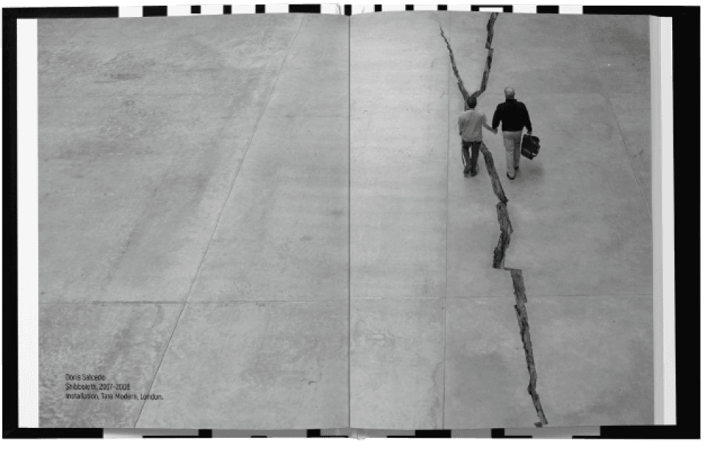 The book open at a full-bleed image spread. One aerial black-and-white photograph of Doris Salcedo’s Shibboleth — the long crack splitting the concrete floor of the Tate Modern turbine hall — runs across the gutter and off all four edges, two figures walking beside it. The credit sits small and grey in the bottom-left corner: Doris Salcedo, Shibboleth, 2007–2008, Installation, Tate Modern, London. No other type is on the spread.